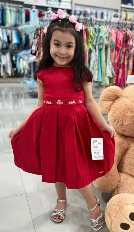 Menina experimentando vestido vermelho dentro da loja Bela Infância